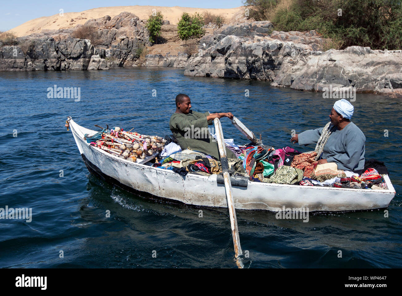 Un negozio di souvenir e un venditore di tessili e di suo figlio racchetta la loro barca verso una imbarcazione turistica sul fiume Nilo vicino a Aswan in Egitto. Foto Stock