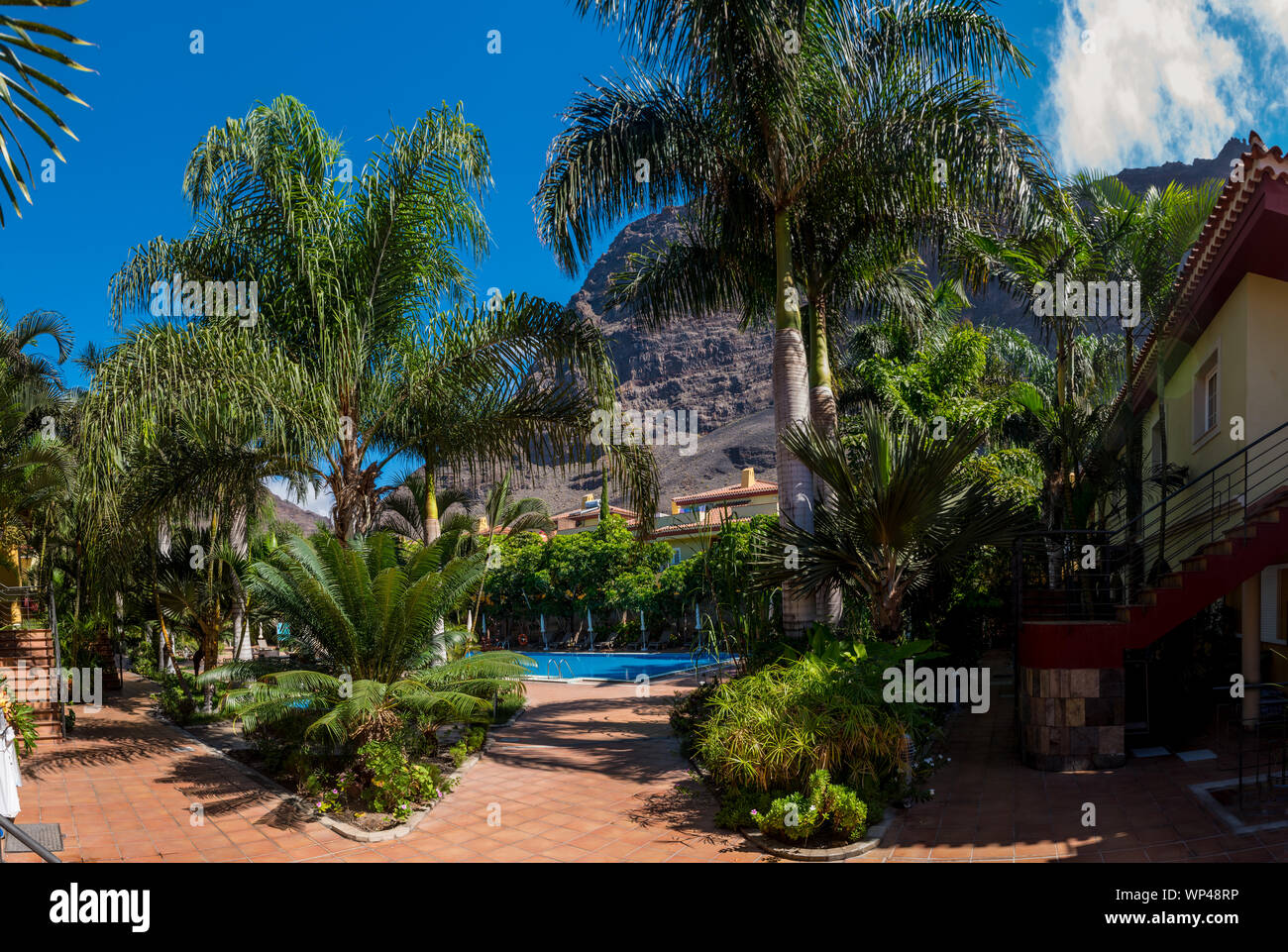 Attraenti giardini semi-tropicali una piscina a la Calera, la Gomera, Isole Canarie con grandi palme, cielo blu e sfondo roccioso di montagna Foto Stock