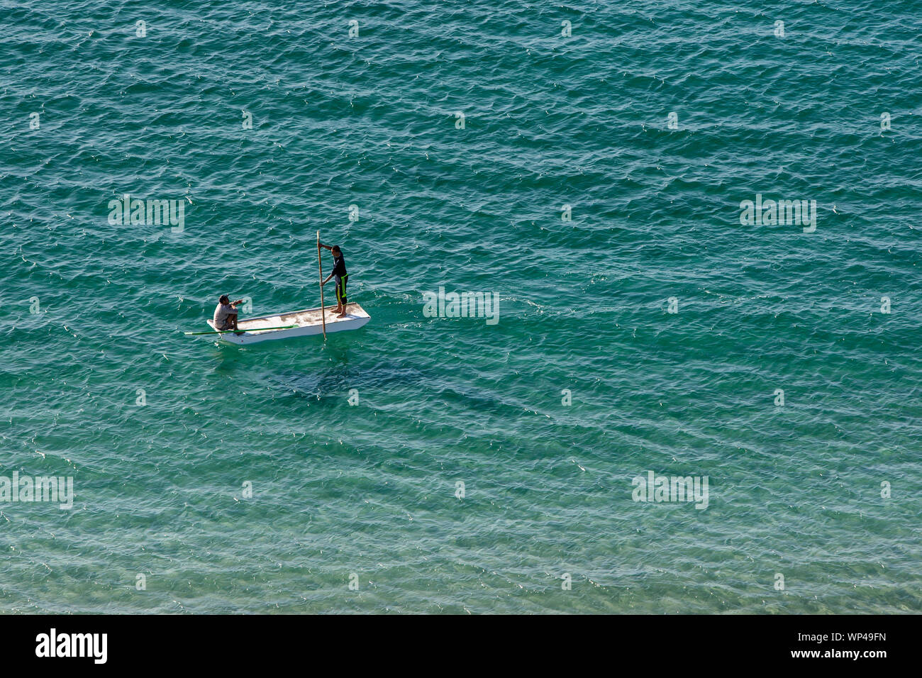 Gli uomini paddle una piccola barca attraverso le acque turchesi del Mar Mediterraneo al largo della costa di Alessandria in Egitto settentrionale. Foto Stock