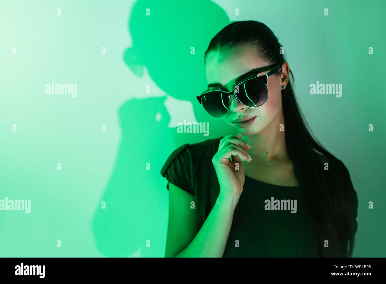 Notte ritratto di una giovane ragazza bella con la riflessione in occhiali da sole nel verde della luce al neon. Foto Stock