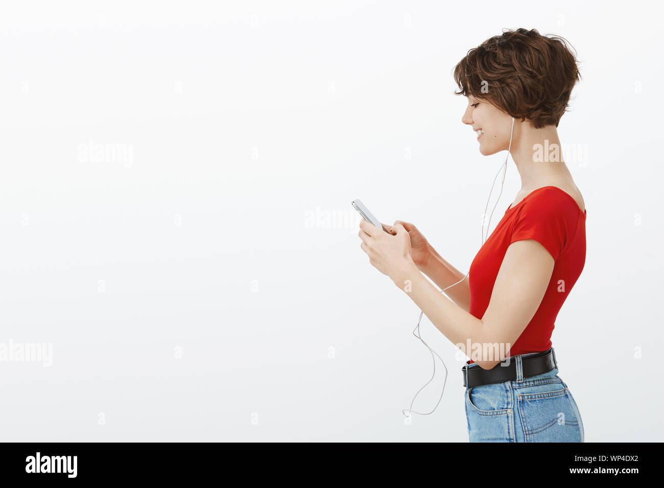 Profilo vivace shot donna moderna ha messo in pista preferita di tenere lo smartphone ascoltare canzoni in piedi alla metropolitana indossare gli auricolari texting amici guardare i video musi Foto Stock