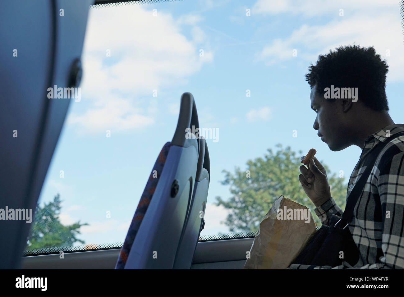Un giovane uomo di mangiare una scatola di pollo fritto su un bus di Londra Foto Stock
