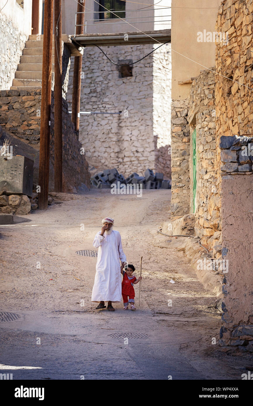 Nonno e bambina tenendo le mani mentre si cammina su una strada idilliaca di un villaggio vicino a Nizwa, Oman Foto Stock