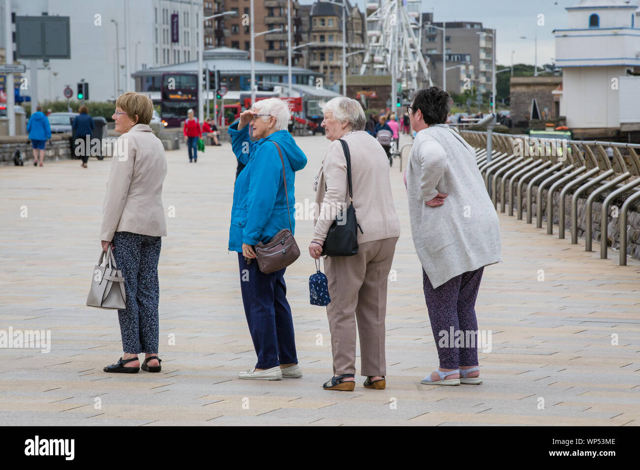 Quattro donne anziane in piedi in una fermata della linea e di guardare qualcosa attraverso la strada in Weston-Super-Mare, Somerset. Regno Unito Foto Stock