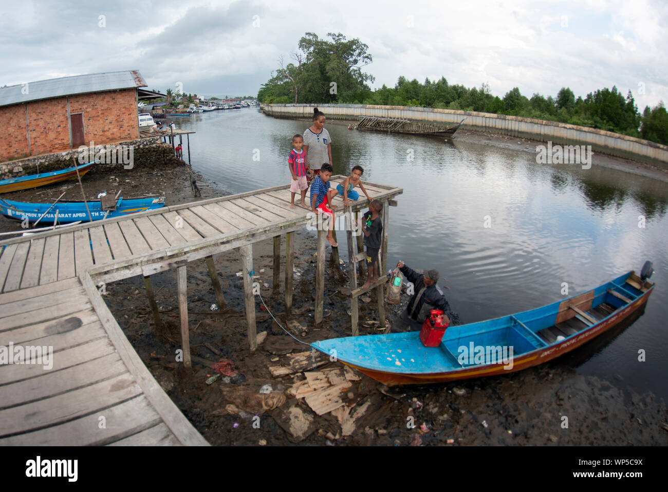 Famiglia lo scarico di merci dalla canoa sul molo sul fiume, Sorong, Papua occidentale, in Indonesia Foto Stock
