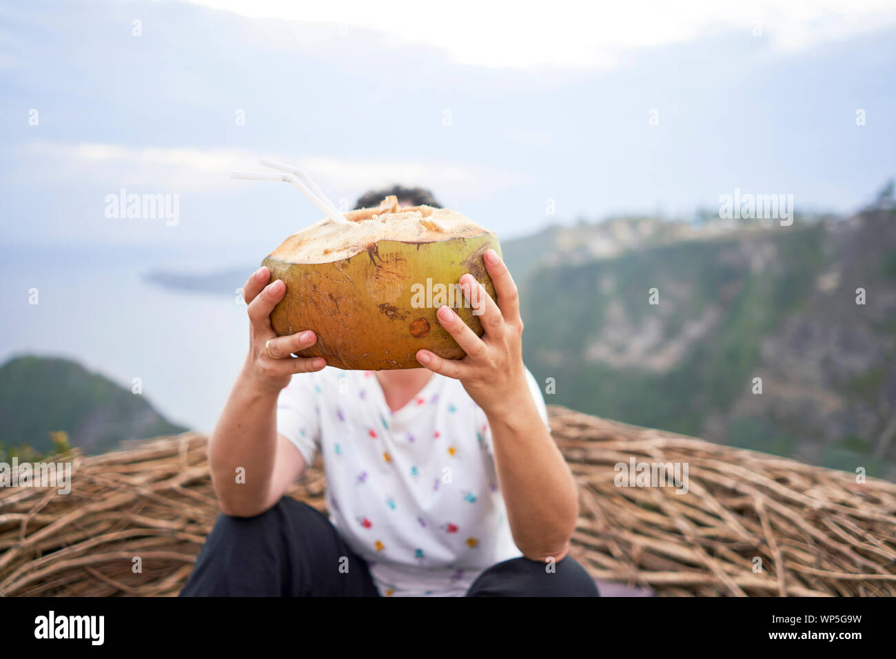 Giovane donna prendendo una pausa e bere una noce di cocco di fronte al mare, Bali, Indonesia Foto Stock