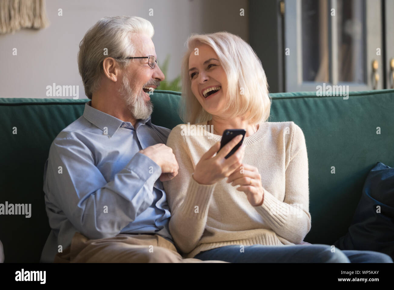 Felice famiglia pensionati ridere utilizza lo smartphone a casa. Foto Stock