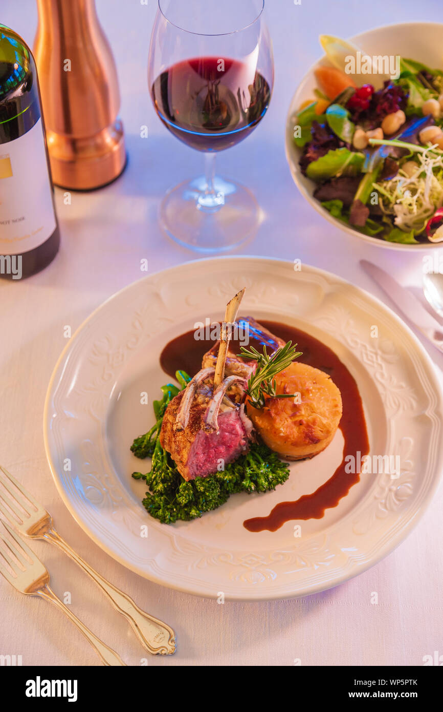 Costolette di agnello su una piastra bianca con un bicchiere di vino rosso. Foto Stock