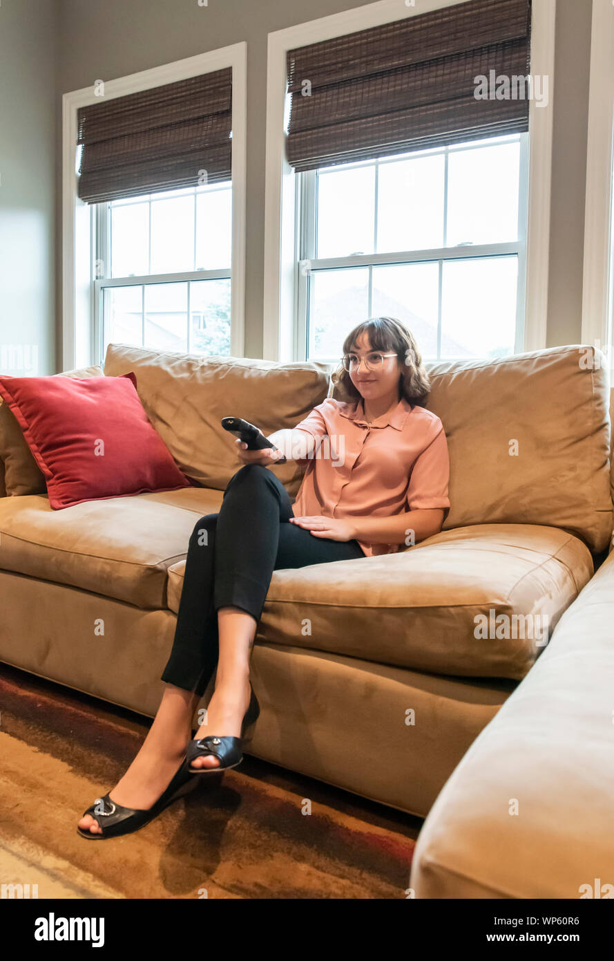 Giovane donna seduta su un divano in abbigliamento business guardando la televisione. Foto Stock
