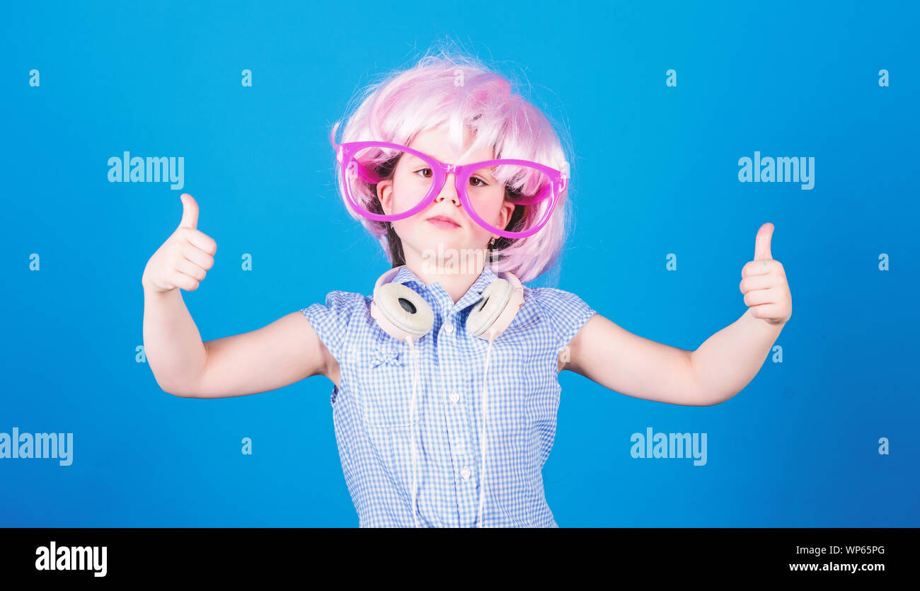 Thumbs up per comode cuffie. Bambina in bicchieri di fantasia che indossa  le cuffie e capelli rosa parrucca. Un bambino piccolo con moderne cuffie  senza fili. Carino kid approvazione auricolari cuffie stereo