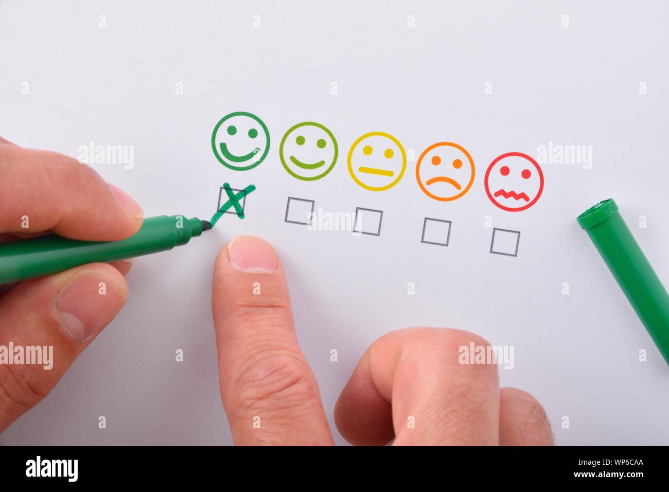 Marcatura a mano un livello di soddisfazione positivo rappresentato con cinque Emoticon colorate su carta bianca. Composizione orizzontale. Vista dall'alto. Foto Stock