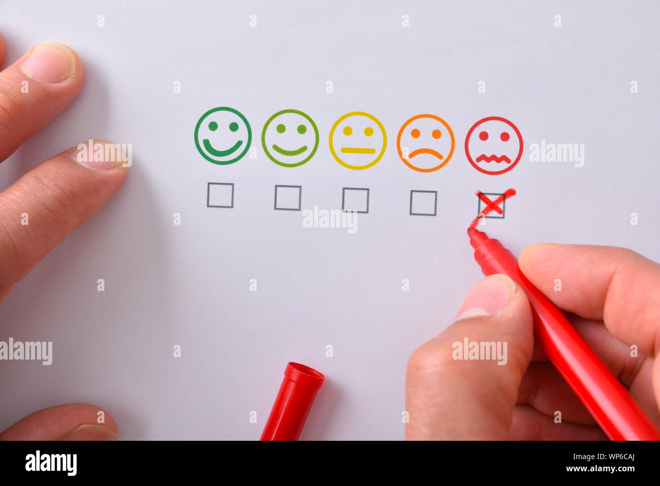 Marcatura a mano un livello di soddisfazione negativa rappresentata con cinque Emoticon colorate su carta bianca. Composizione orizzontale. Vista dall'alto. Foto Stock