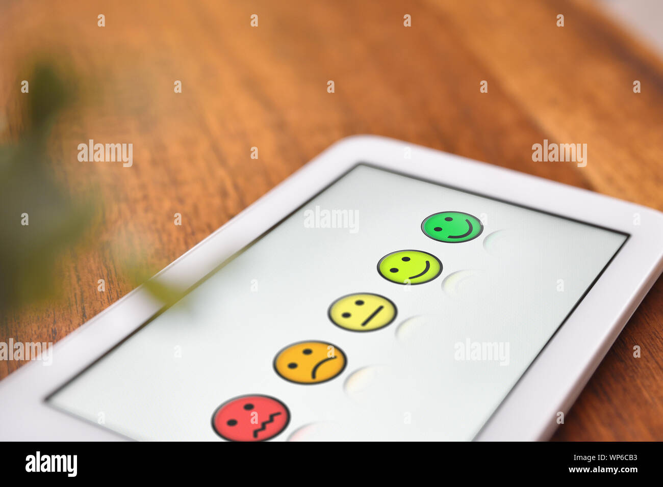 Soddisfazione dei livelli di rappresentazione con le emoticon su bianco tablet schermo sul tavolo di legno vicino. Composizione orizzontale. Vista in elevazione. Foto Stock