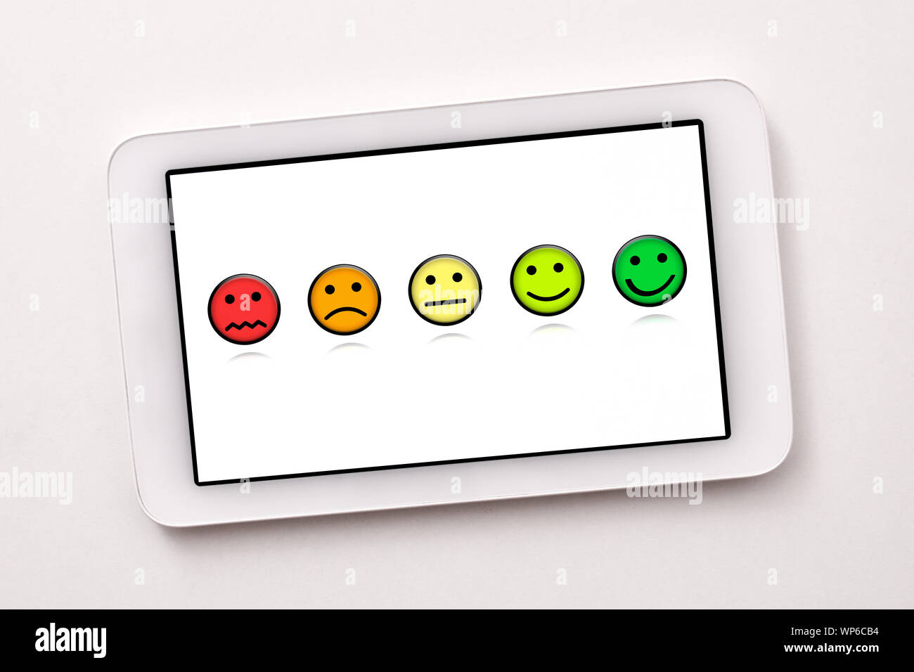 Soddisfazione dei livelli di rappresentazione con le emoticon su bianco tablet schermo sul tavolo bianco vicino. Composizione orizzontale. Vista dall'alto. Foto Stock
