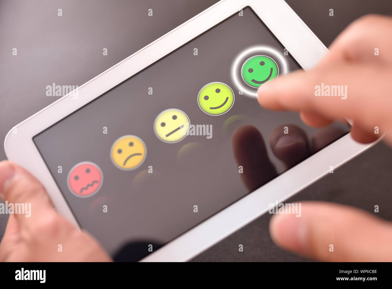 L'uomo valorizzare un servizio su un dispositivo con le emoticon su schermo nero. Composizione orizzontale. Vista dall'alto. Foto Stock