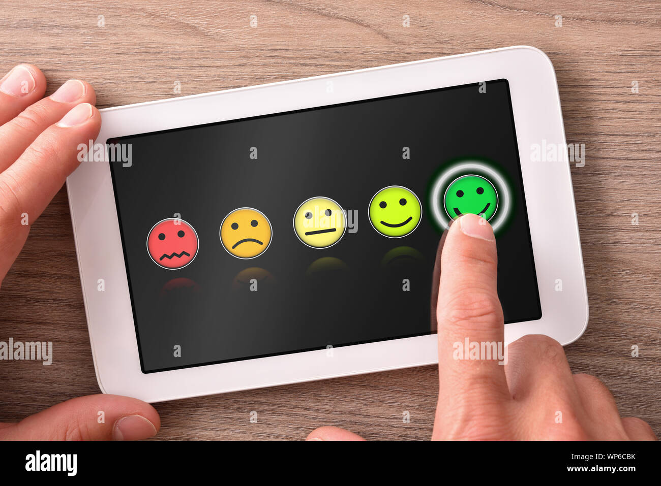 Valutazione positiva su tablet sul tavolo di legno con una rappresentanza di Emoticon colorate su sfondo scuro. Composizione orizzontale. Vista dall'alto. Foto Stock
