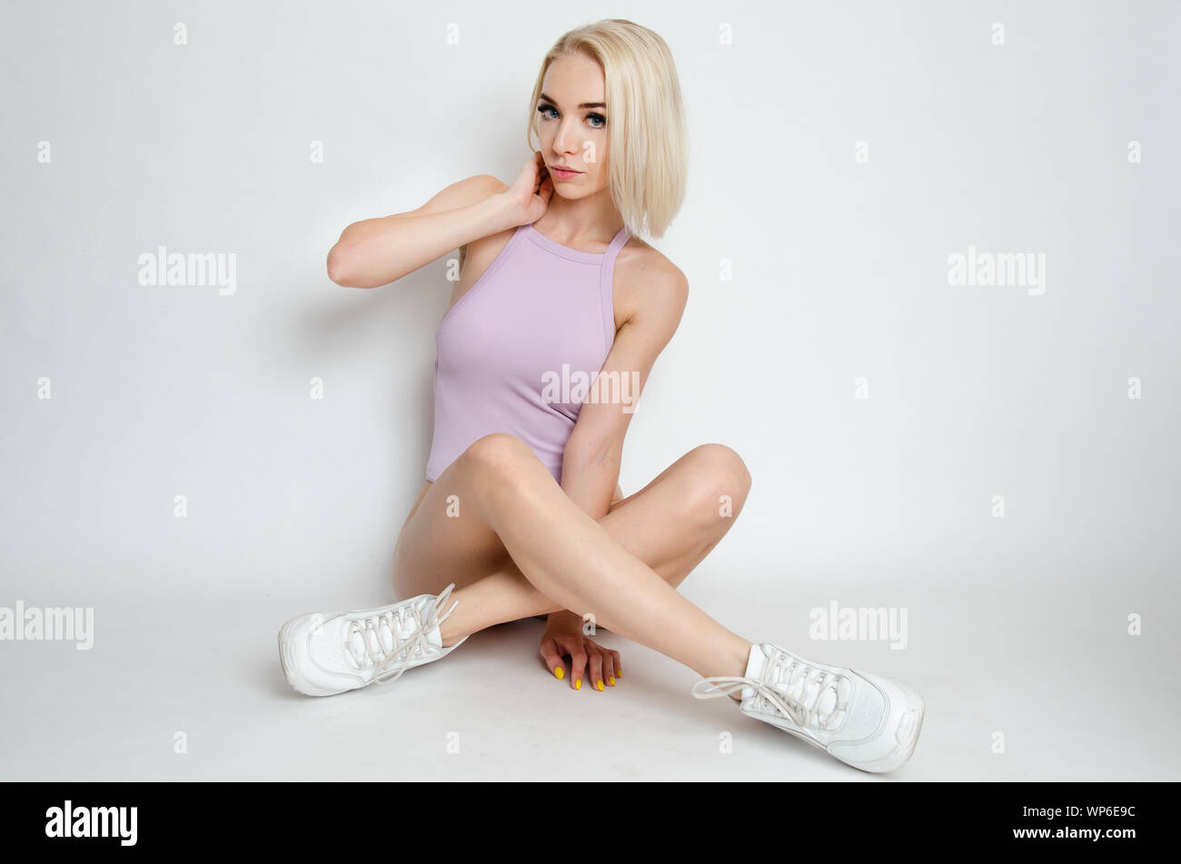 Montare la ragazza seduta sul terreno. Modello femminile dalla Polonia con corpo viola e bianco scarpe sportive. Foto Stock