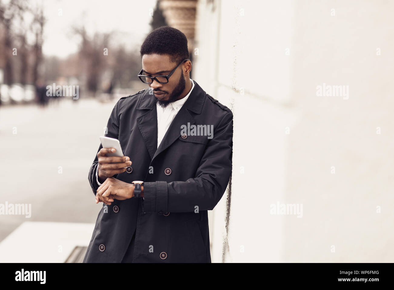 Imprenditore Afro controllo sul tempo di orologi e utilizzando il telefono Foto Stock