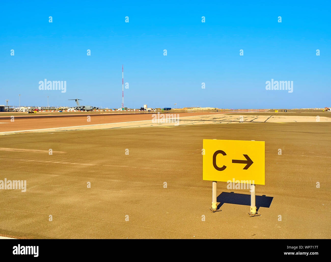 Una pista di un aeroporto con un aereo militare in background e una pista di rullaggio Posizione segno in primo piano. Foto Stock