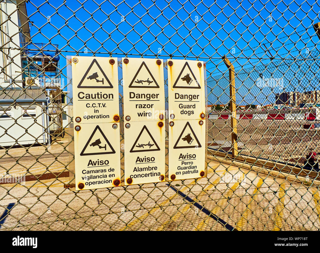 Pericolo e segnali di attenzione in inglese e in spagnolo su una maglia di filo di acciaio a parete di recinzione. Foto Stock