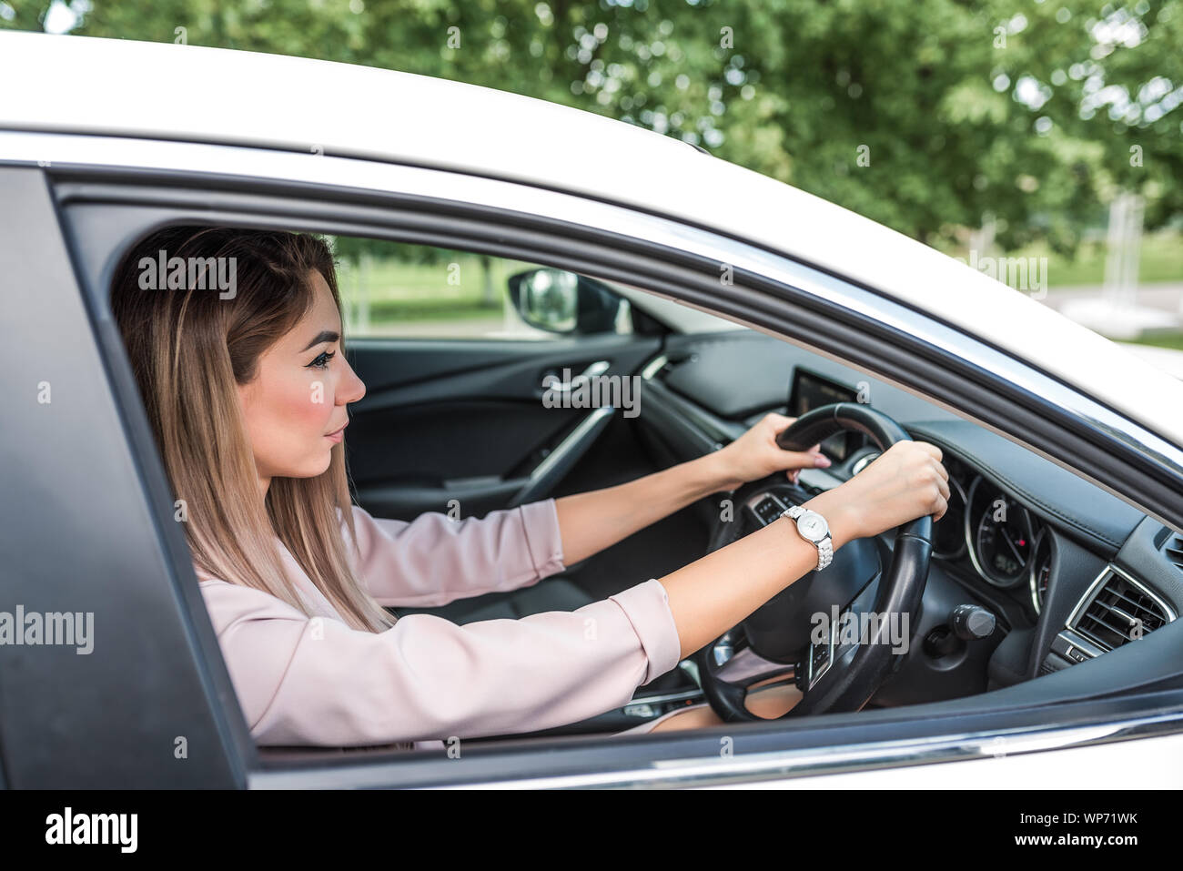 Bella donna d'affari lady è alla guida di un veicolo con guida a destra e a sinistra, estate in città, lo sfondo di alberi e fogliame. Una rigorosa rosa Foto Stock