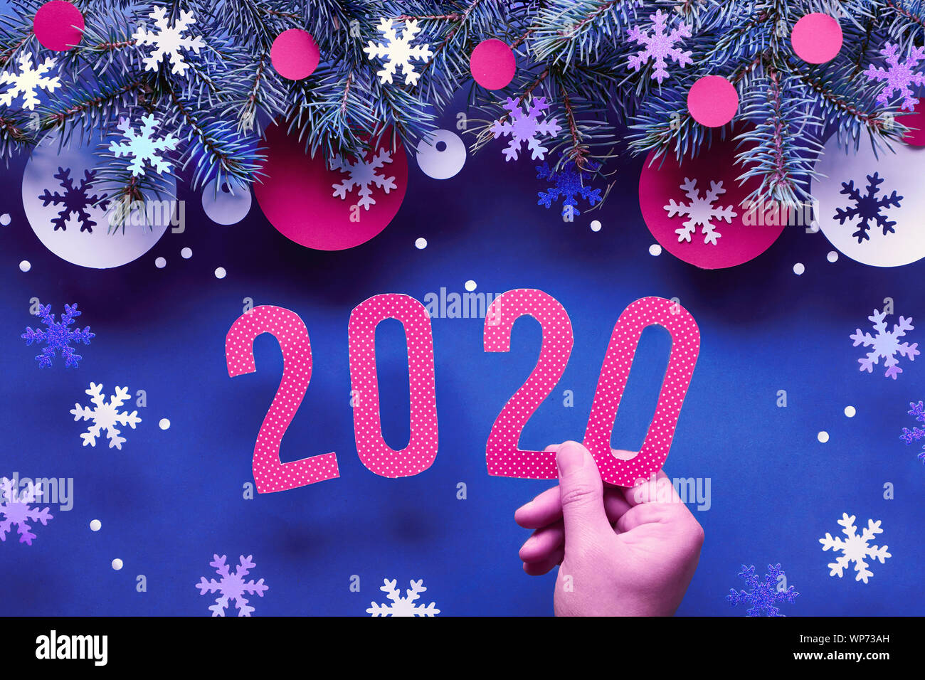 Mano azienda numero 2020, neon sullo sfondo di Natale con ramoscelli di abete rosso e bianco decorazioni di carta. Appartamento laico, vista dall'alto sul blu scuro lo sfondo della carta. Foto Stock