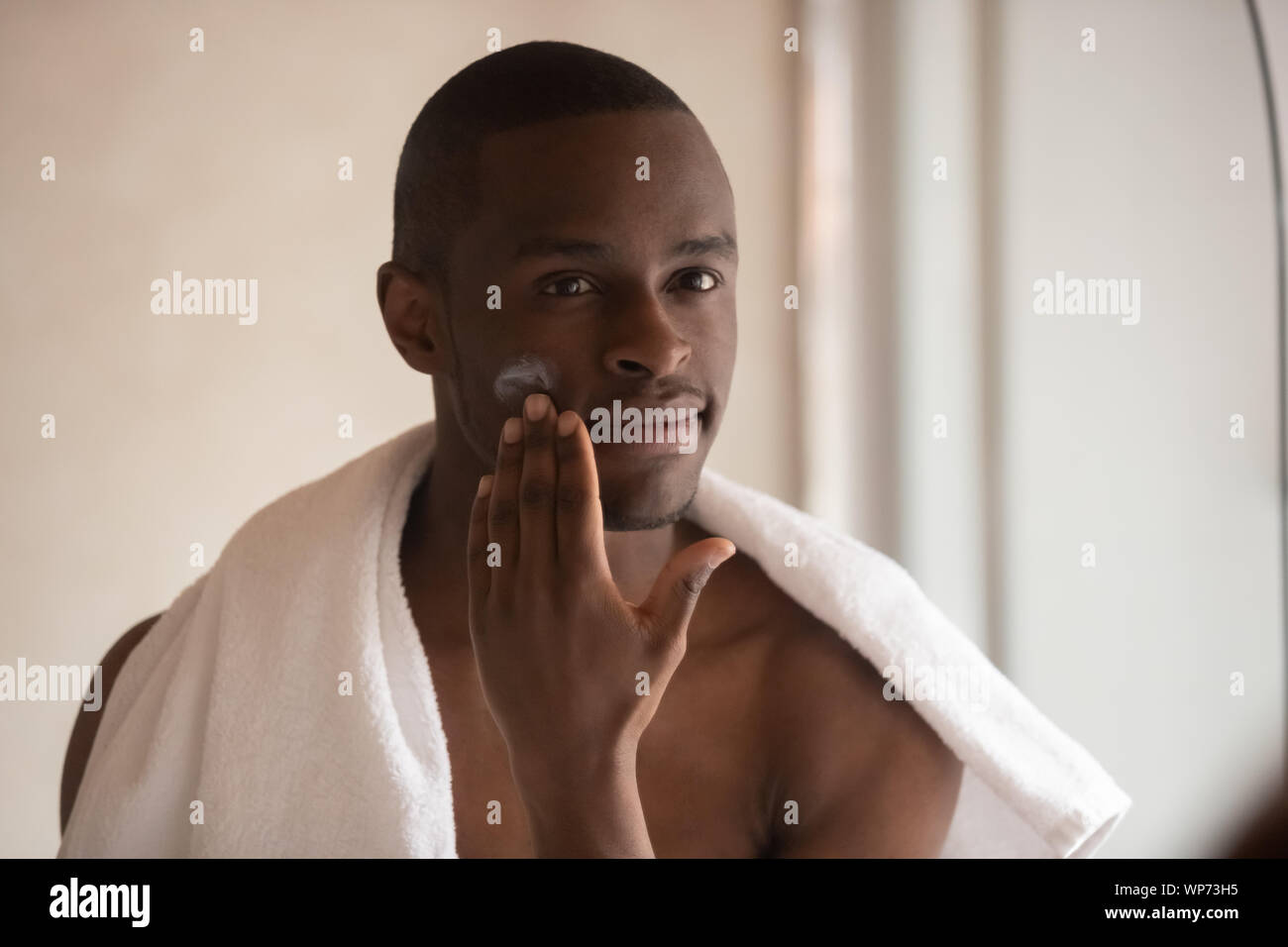 Giovane uomo biracial applicare la crema per il viso dopo la doccia Foto Stock