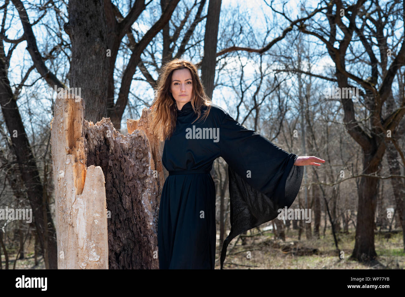 Giovani Tall Woman con scuri capelli lunghi in black robes nel profondo della foresta. Streghe. Halloween e concezione gotica. La stregoneria e magia. Foto Stock