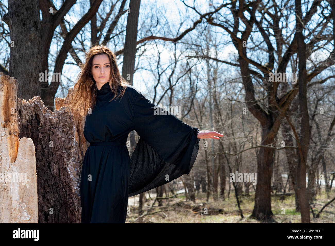 Giovani Tall Woman con scuri capelli lunghi in black robes nel profondo della foresta. Streghe. Halloween e concezione gotica. La stregoneria e magia. Foto Stock