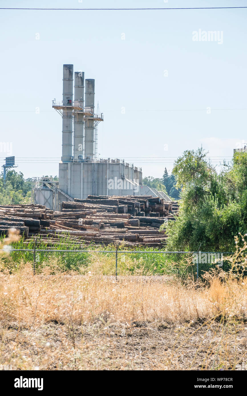 Un grande mulino di legname nel sud della Oregon con tre grandi pile di fumo e plles di tronchi di alberi pronti per l'elaborazione in primo piano. Foto Stock