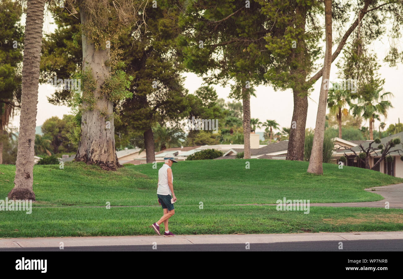 Fotografia analogica di una donna più anziana per la sua passeggiata mattutina con le cuffie sulle orecchie di lei da un campo da golf a Sun City, in Arizona. Foto Stock