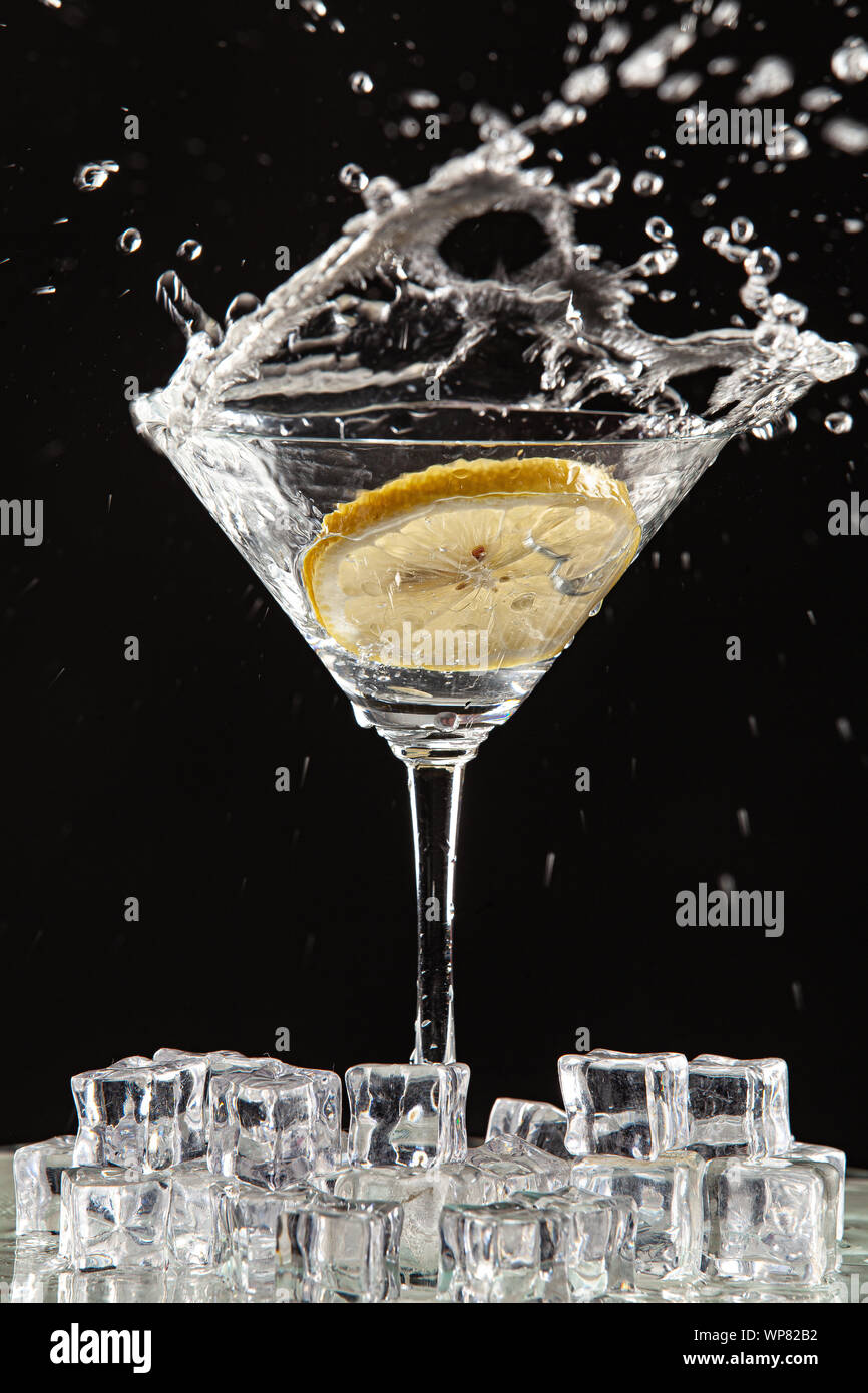 Bicchiere di acqua e limone e watersplashes su un nero di sfondo per studio Foto Stock