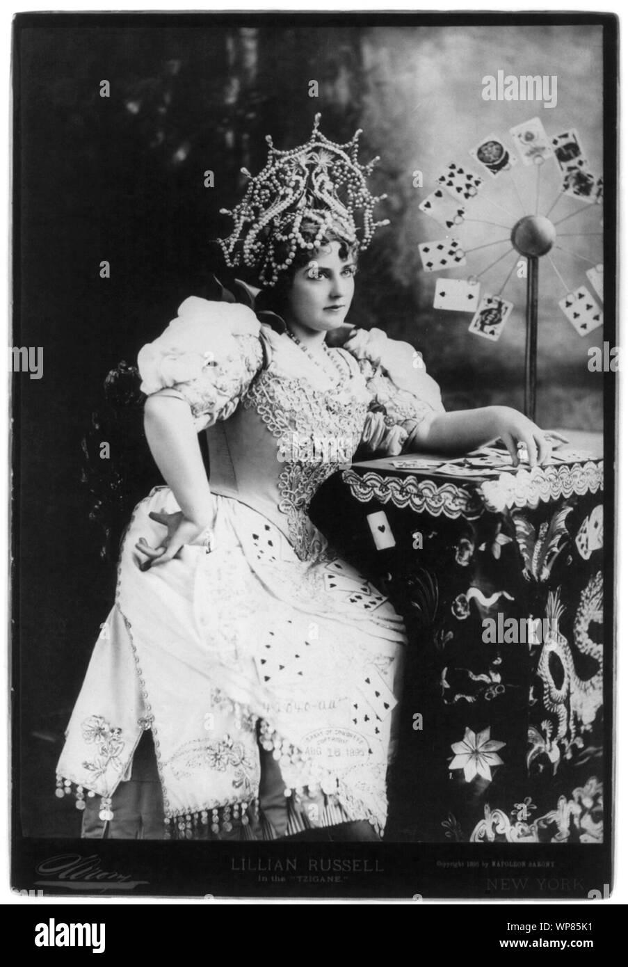 Lillian Russell, 1861-1922, tre quarti di lunghezza, seduto, rivolto verso destra; con le carte in tavola, in Tzigane (fortune teller) Foto Stock