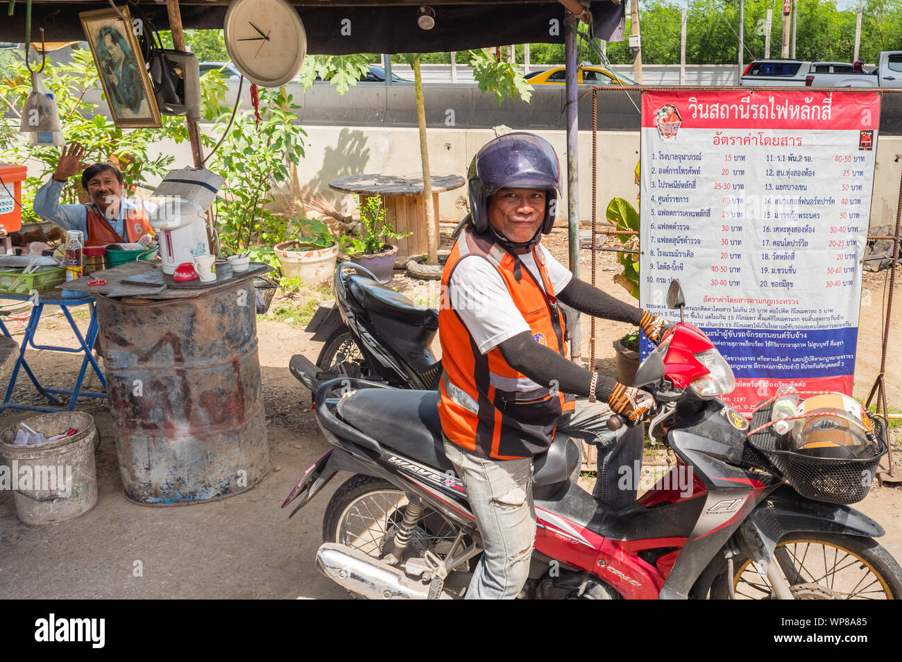 Bangkok - Luglio 11, 2019: una moto taxi driver sorrisi per la fotocamera a una bicicletta alla fermata dei taxi accanto a Lak Si stazione ferroviaria. Foto Stock