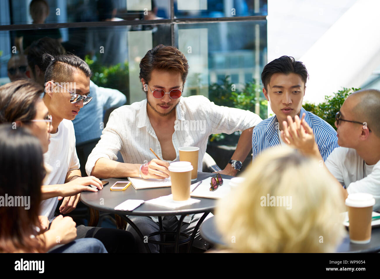 Giovani asiatici studenti del college avente una discussione di gruppo in corrispondenza di un outdoor coffee shop Foto Stock