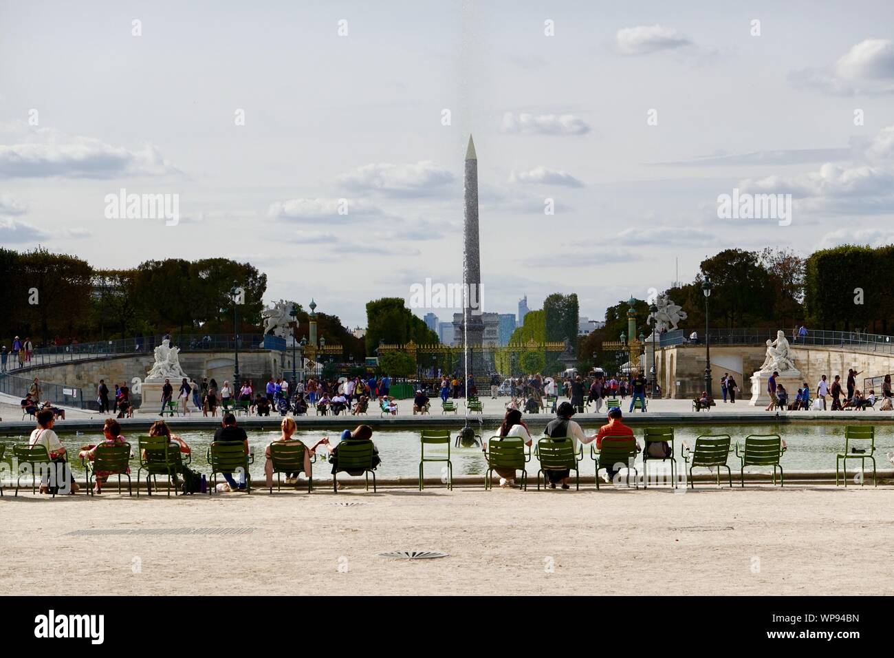 Persone sedute in sedie verde intorno al bacino ottagonale all'estremità occidentale dei Giardini Tuileries, l'obelisco egizio nel posteriore, Paris, Francia. Foto Stock