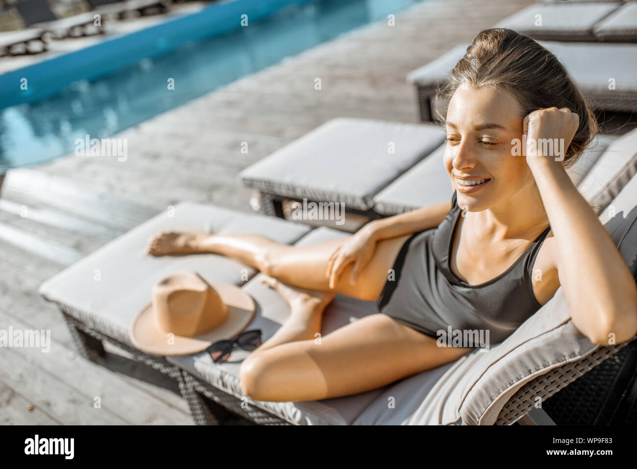 Donna in costume nero sdraiato sul lettino vicino alla piscina all'aperto. prendere il sole su un tempo di estate Foto Stock