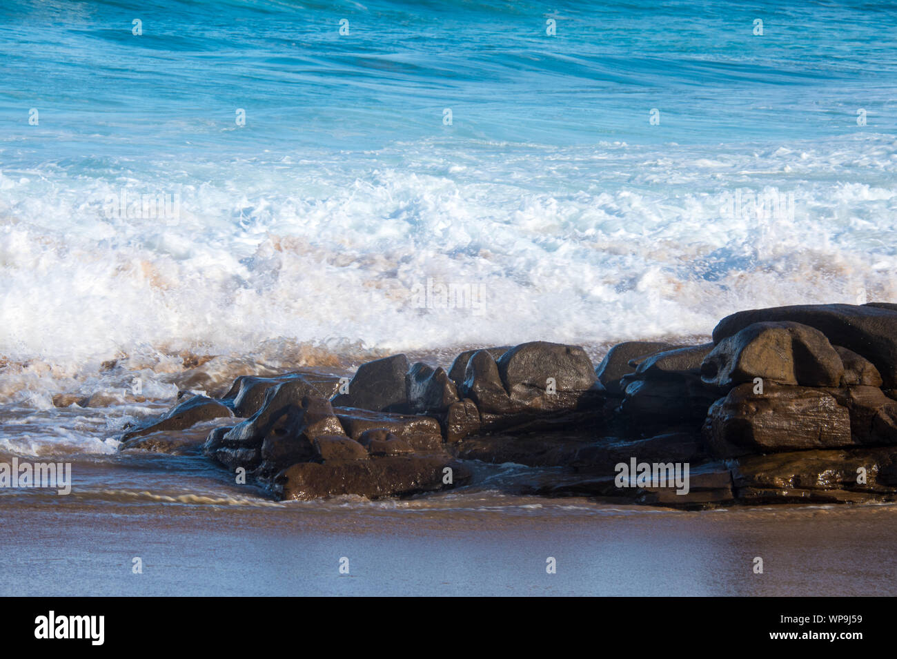 Marea. Seascape colorato. Vicious onde che si schiantano contro il litorale su un pomeriggio soleggiato. Vi è una piccola coltura roccioso in primo piano Foto Stock