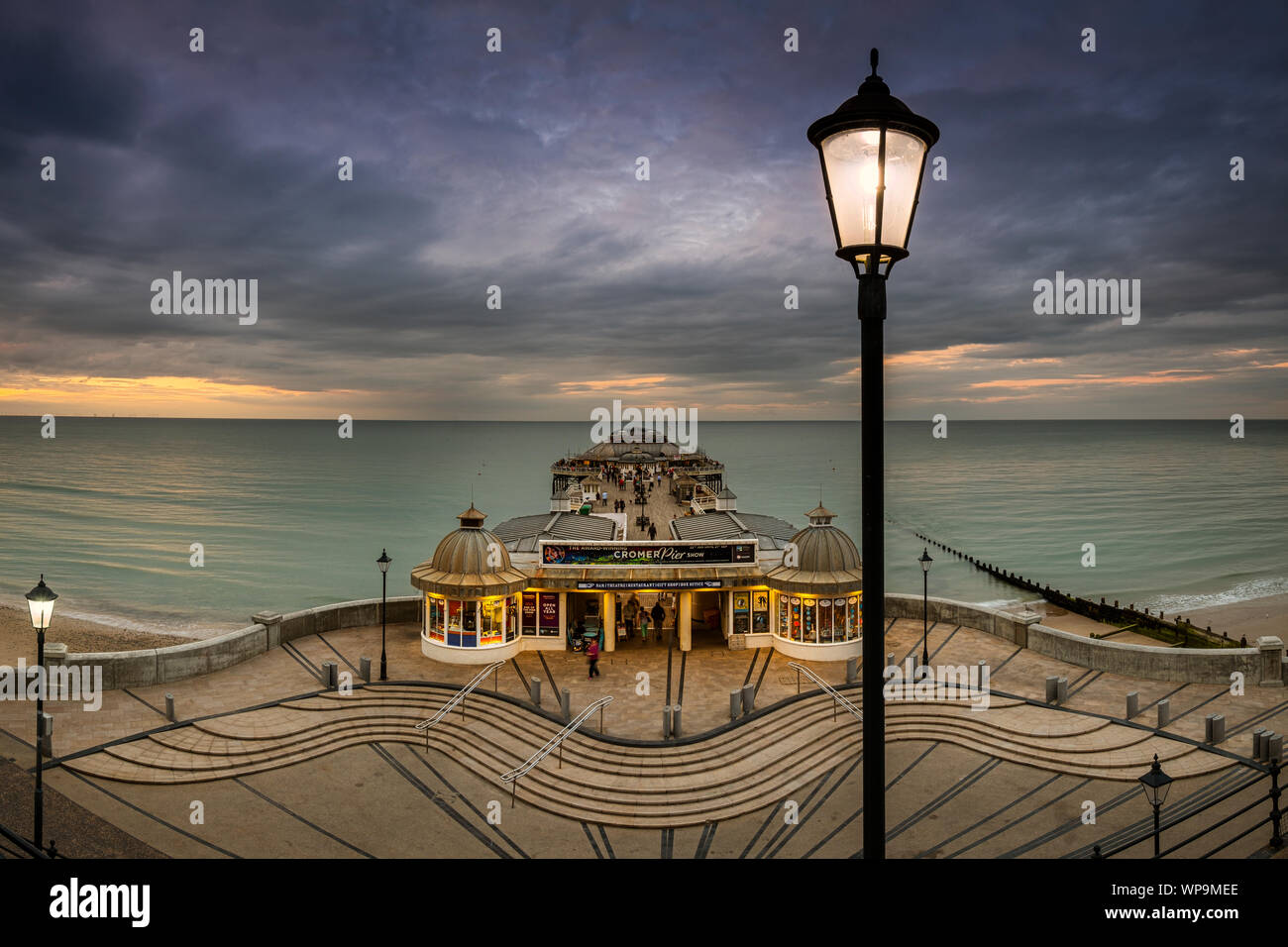 Le luci di strada iniziano a venire su come il sole tramonta a Cromer Pier. Foto Stock