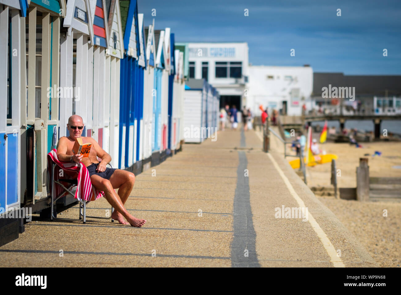 Un uomo seduto in una sedia pieghevole in sun readng un libro al mare. Foto Stock