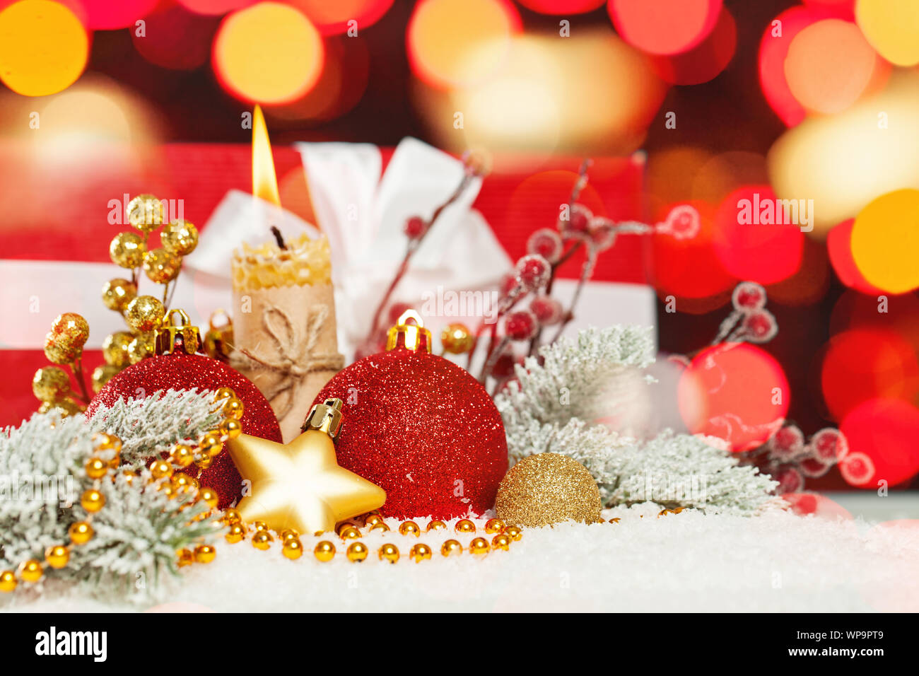 Colorata composizione di Natale con abstract bokeh sfondo chiaro, verde abete natalizio il ramo, oro garland, rosso baubles, agrifoglio bacche e candela su whi Foto Stock