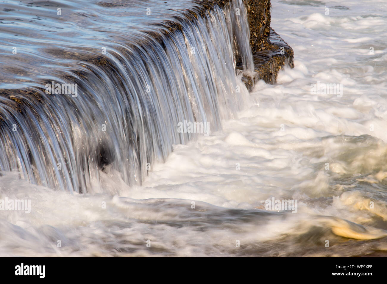 Pomeriggio Un forte, marea. Le onde sono di schiantarsi su una marea di parete della piscina e creando un potente flusso di ritorno. Surf schiumoso e potenti flussi di crash Foto Stock