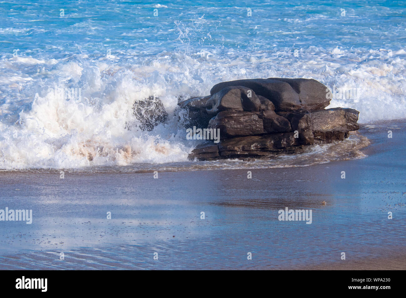 Marea. Vicious onde con la marea di schiantarsi contro il litorale con una forte risacca. Il surf è schiumoso nel sole del pomeriggio. Foto Stock