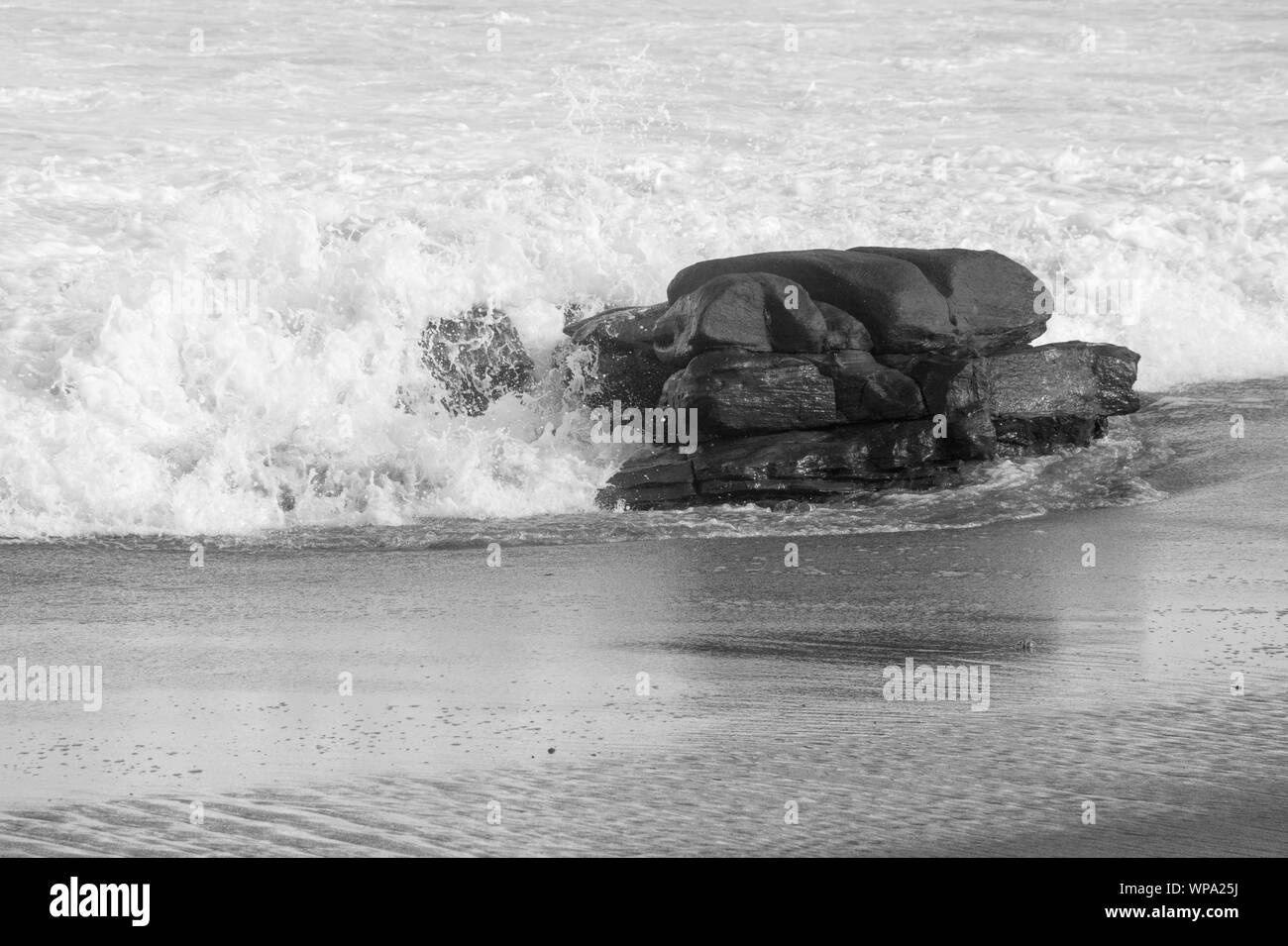 Un bel bianco e nero seascape con serena e spumeggianti acque. Le onde si infrangono contro una roccia nel tardo pomeriggio. Foto Stock