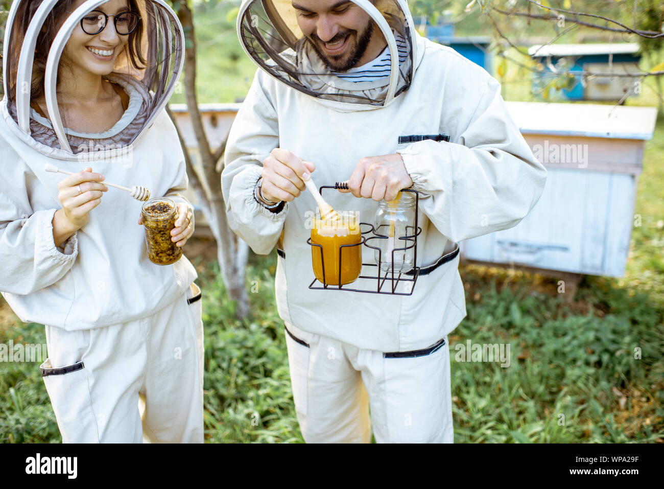 Due beekepers in uniforme di protezione in piedi insieme con il miele nel vaso, la degustazione di prodotto fresco sull'apiario all'aperto Foto Stock
