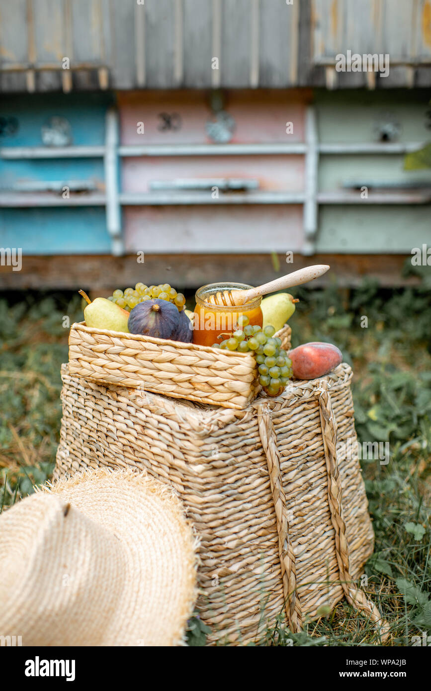 Composizione di frutti dolci e vaso pieno di miele con mobilia di legno alveari sullo sfondo all'apiario Foto Stock