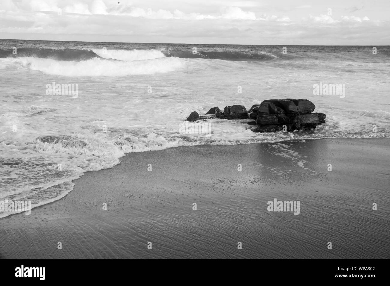 Un bel bianco e nero seascape con serena e spumeggianti acque. Le onde si infrangono contro una roccia nel tardo pomeriggio. Foto Stock