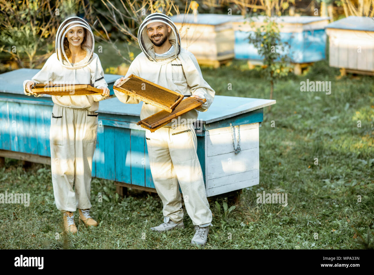 Due gli apicoltori in uniforme di protezione a piedi con favi mentre si lavora su una tradizionale apiario. Concetto di apicoltura e le piccole aziende agricole Foto Stock