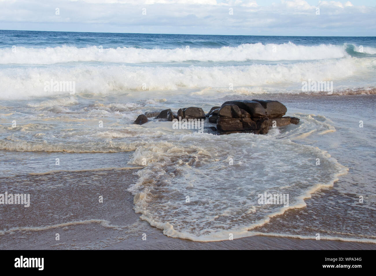 Marea. Vicious onde con la marea di schiantarsi contro il litorale con una forte risacca. Il surf è schiumoso nel sole del pomeriggio. Foto Stock