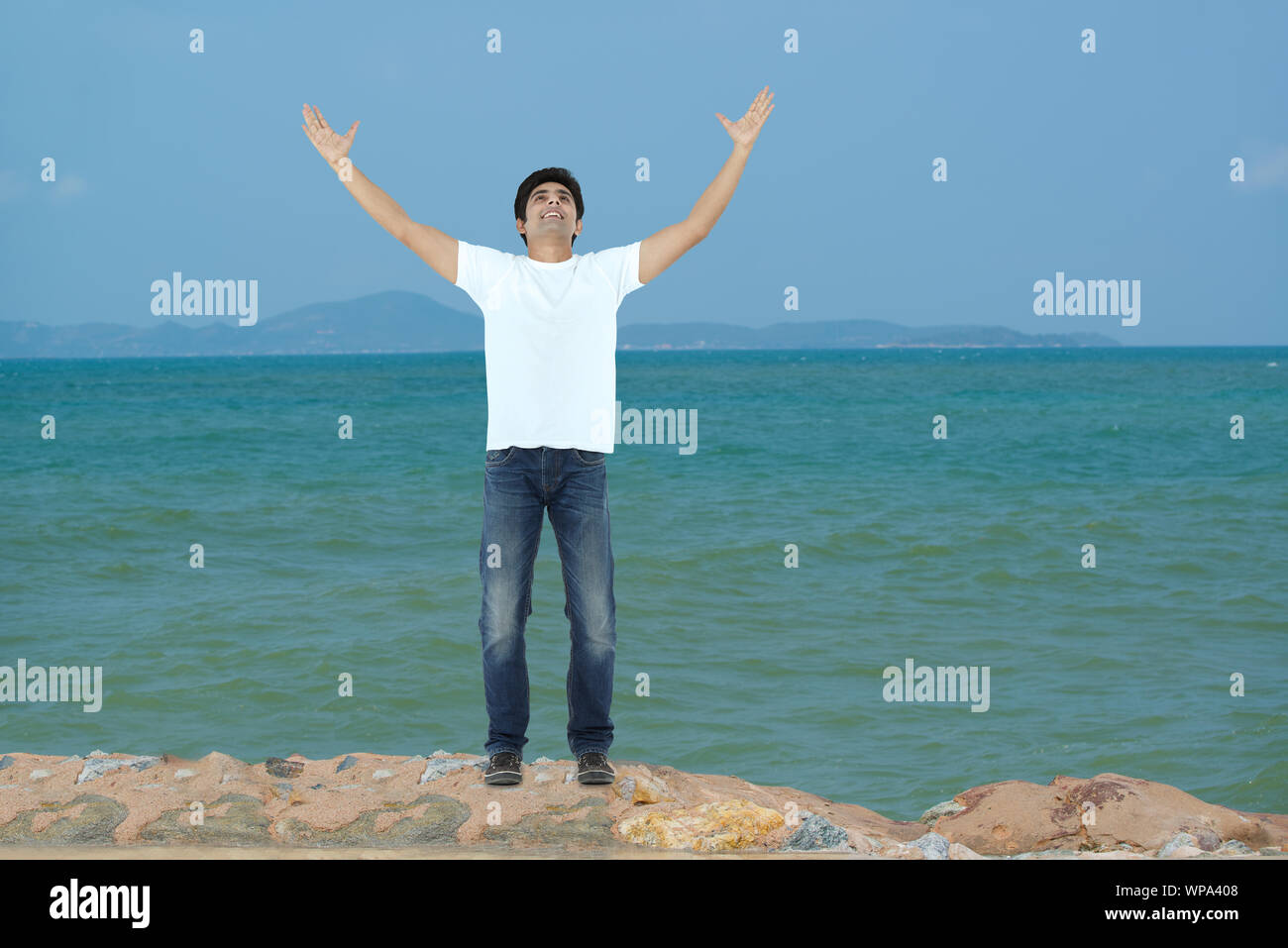 Giovane uomo in piedi con il braccio teso sulla costa Foto Stock